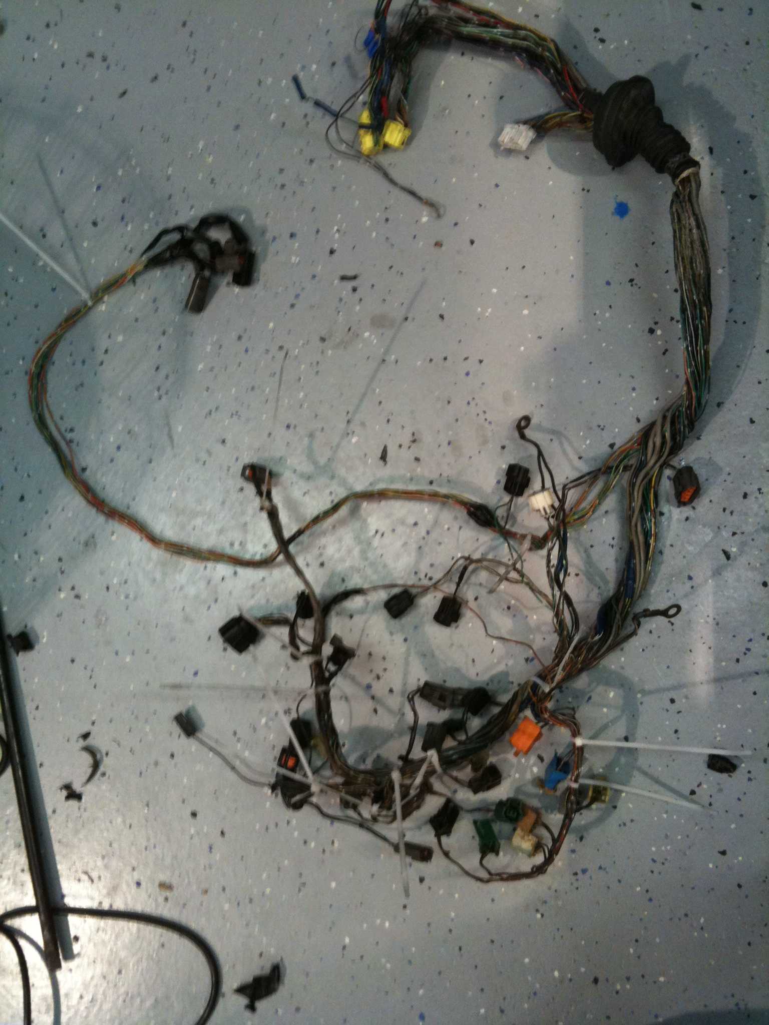 A removed wiring harness with multiple colored wires and connectors laid out on a speckled floor