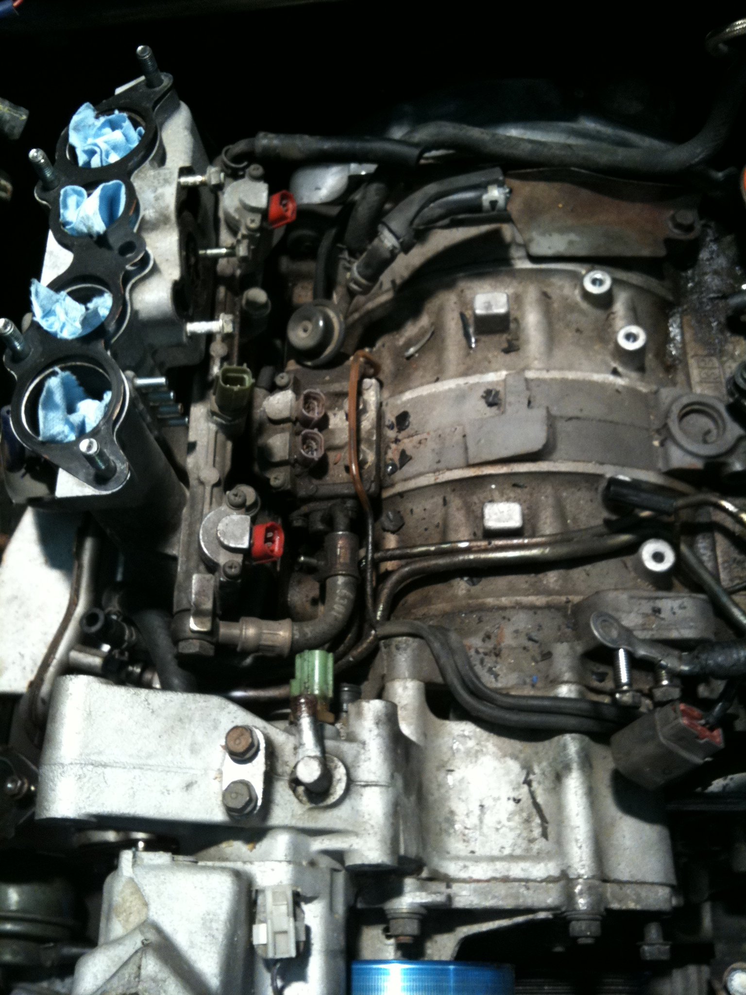 Close-up of an engine intake manifold with blue rags stuffed in ports, metallic gray tones