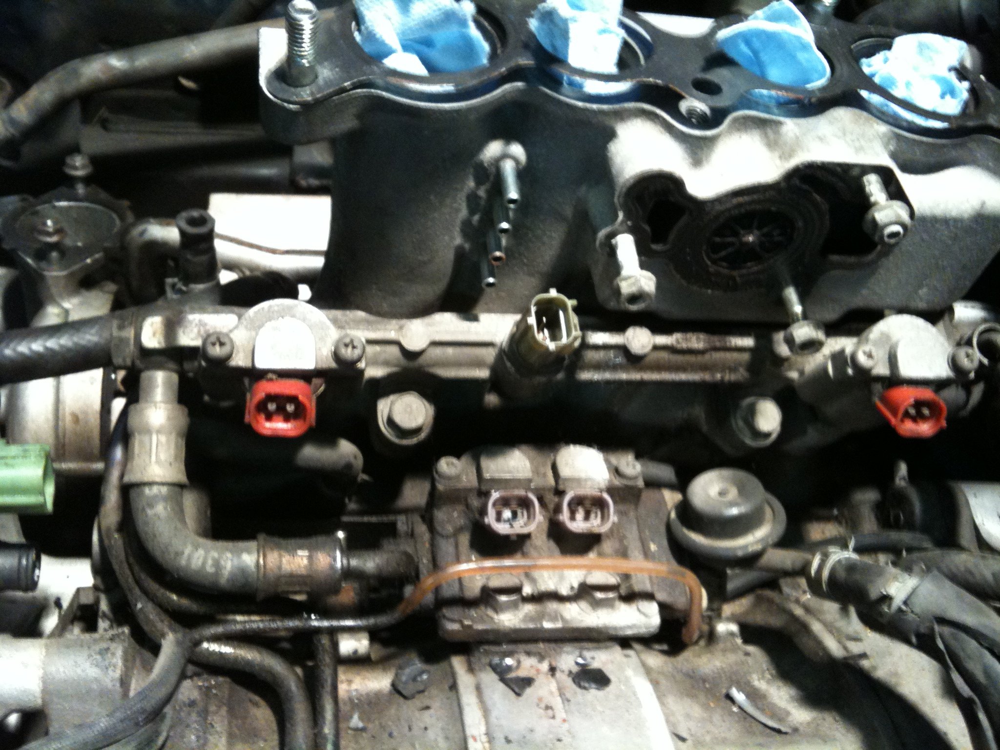 Close-up of engine fuel rail and injectors with blue rags in intake ports, red and gray connectors