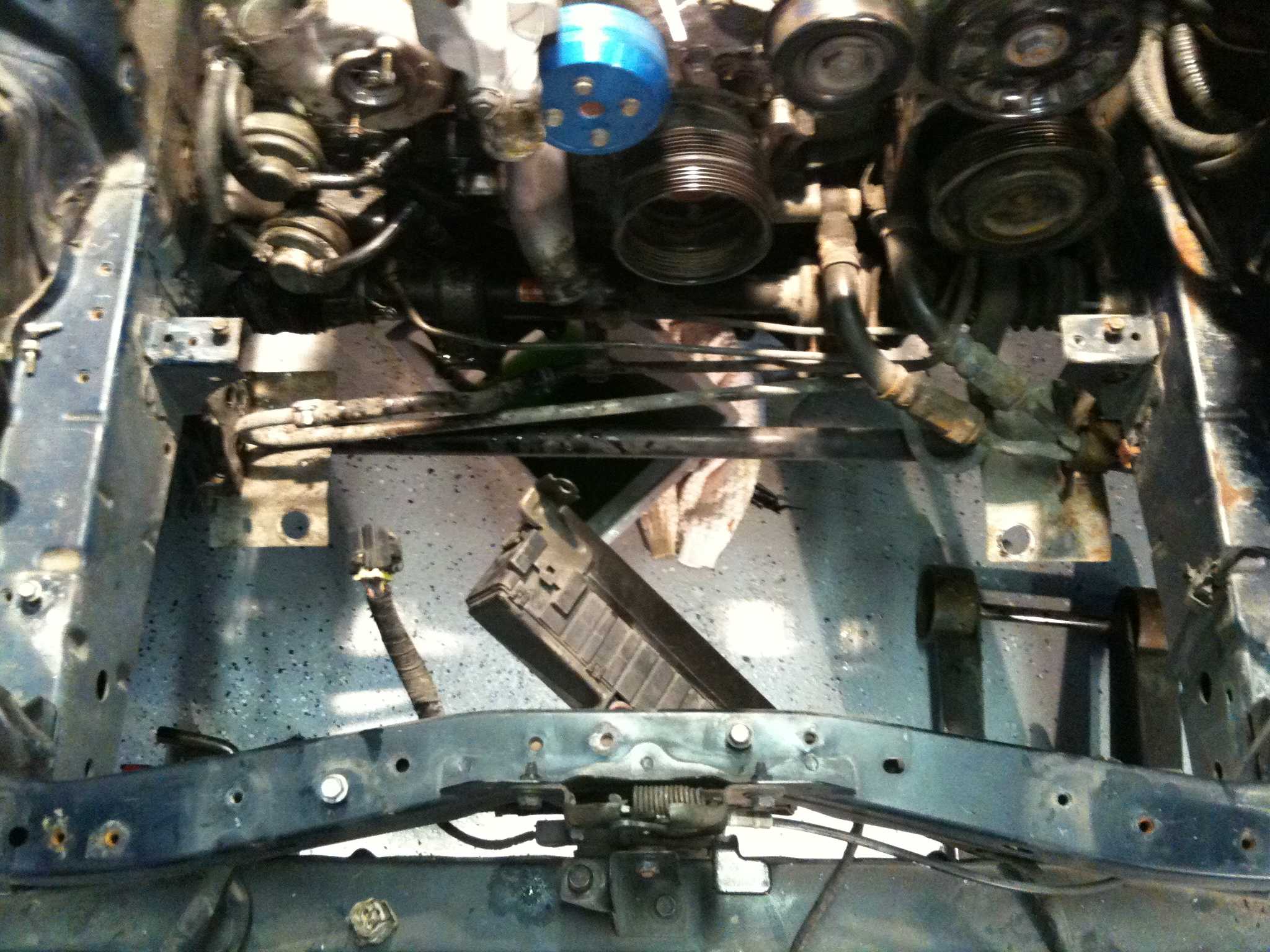 Bold charcoal drawing of an engine bay from above showing pulleys, hoses, and chassis rails, moody gray and blue tones, mechanical atmosphere
